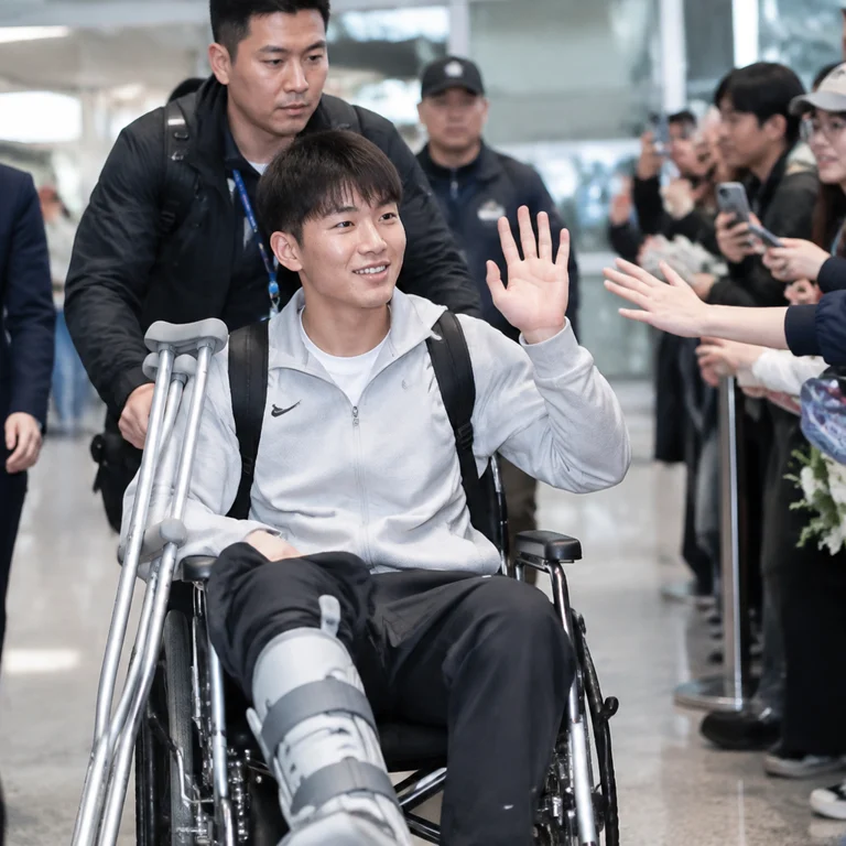 毛伟杰受伤后坐轮椅抵达,向现场接机球迷挥手致意